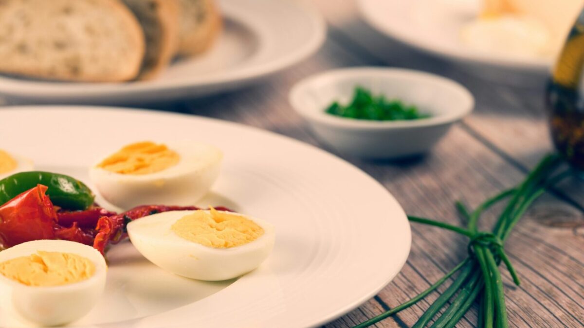 Delicious homemade sliced boiled eggs served with herbs and vegetables on a rustic wooden table.