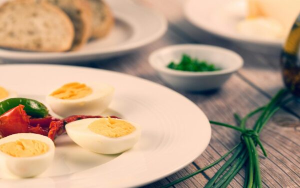 Delicious homemade sliced boiled eggs served with herbs and vegetables on a rustic wooden table.