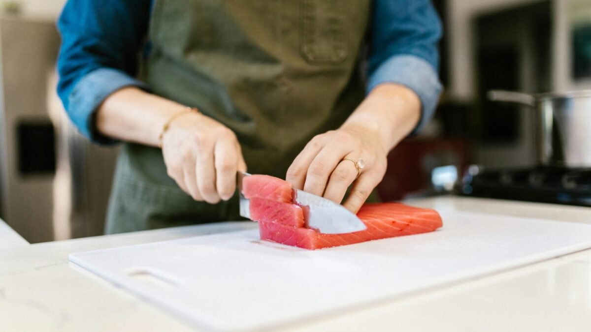 Close-up of a person slicing fresh salmon fillets on a cutting board, showcasing culinary skills in a home kitchen.