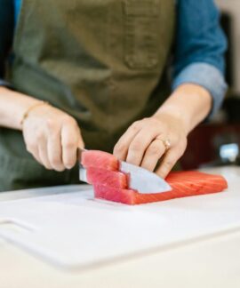 Close-up of a person slicing fresh salmon fillets on a cutting board, showcasing culinary skills in a home kitchen.