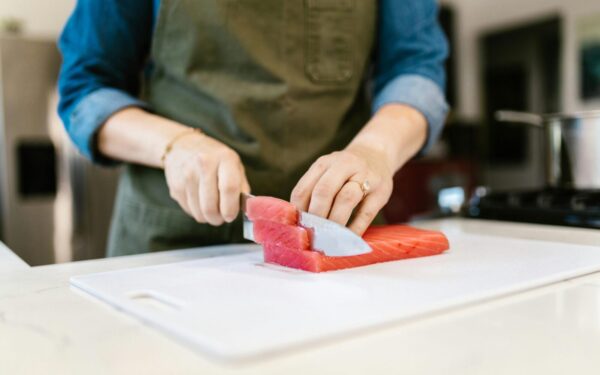 Close-up of a person slicing fresh salmon fillets on a cutting board, showcasing culinary skills in a home kitchen.
