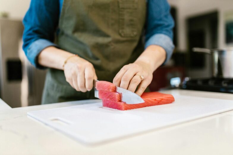 Close-up of a person slicing fresh salmon fillets on a cutting board, showcasing culinary skills in a home kitchen.
