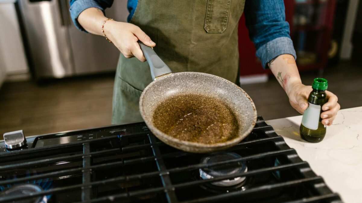 Chef holding frying pan with olive oil in kitchen, ready to cook a delicious meal.
