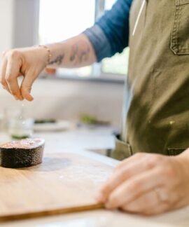 Close-up of a tattooed chef seasoning a salmon steak with salt in a modern kitchen.