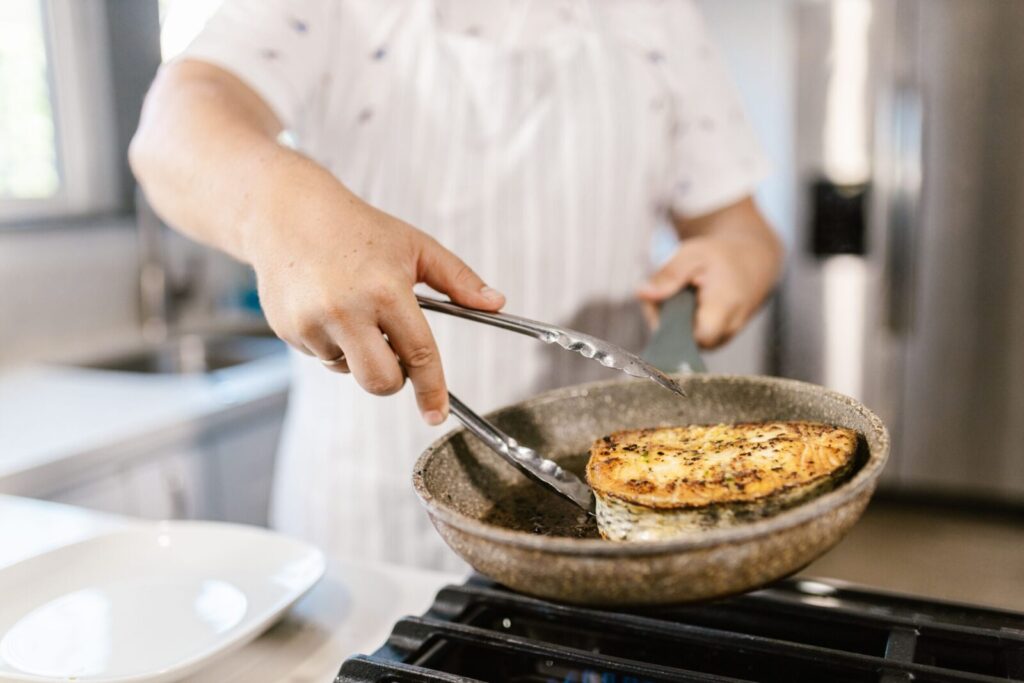 A chef cooking seasoned fish fillet in a frying pan in a modern kitchen.
