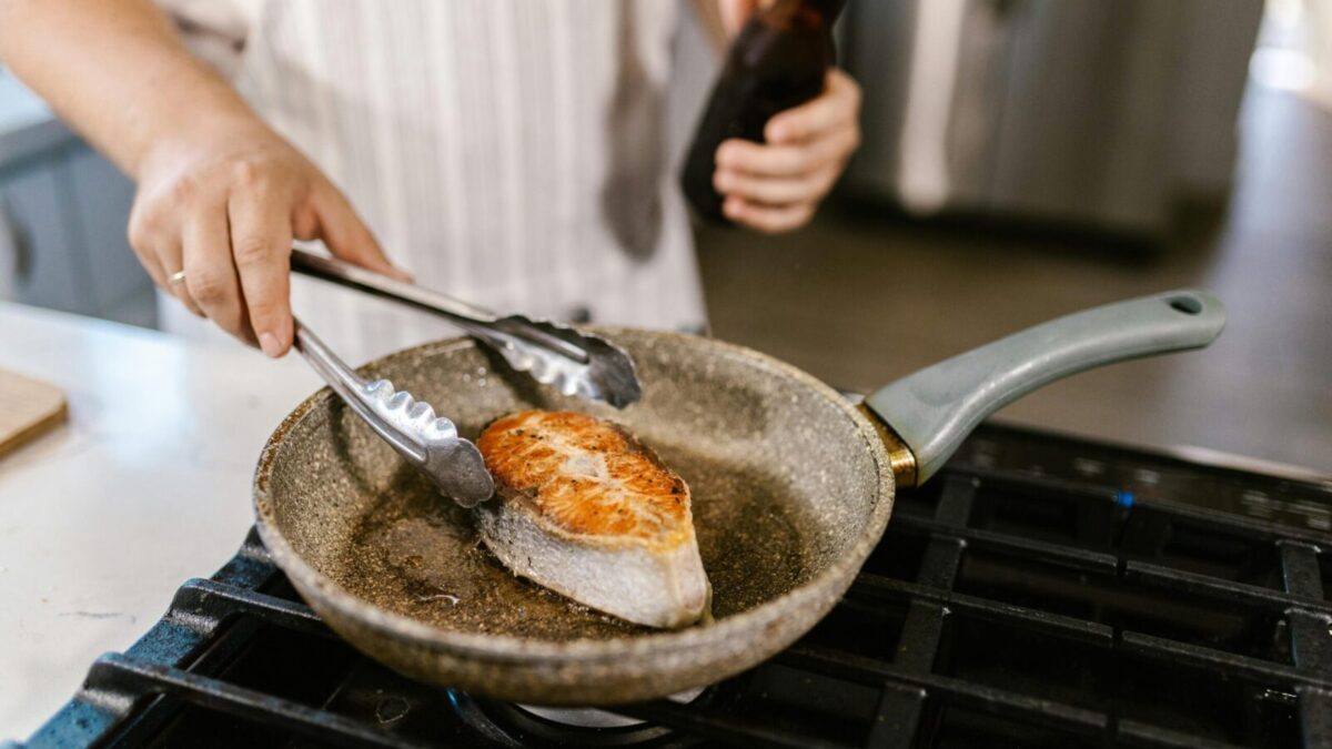 A close-up shot of a salmon steak being grilled in a non-stick pan in a kitchen setting. Perfect for cooking enthusiasts.