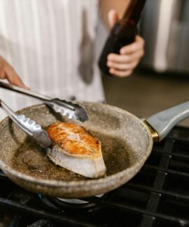 A close-up shot of a salmon steak being grilled in a non-stick pan in a kitchen setting. Perfect for cooking enthusiasts.