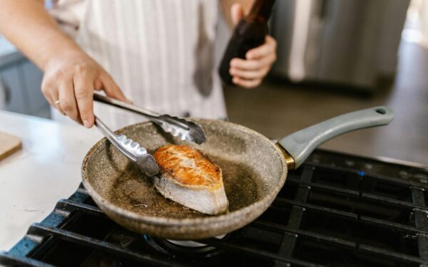 A close-up shot of a salmon steak being grilled in a non-stick pan in a kitchen setting. Perfect for cooking enthusiasts.