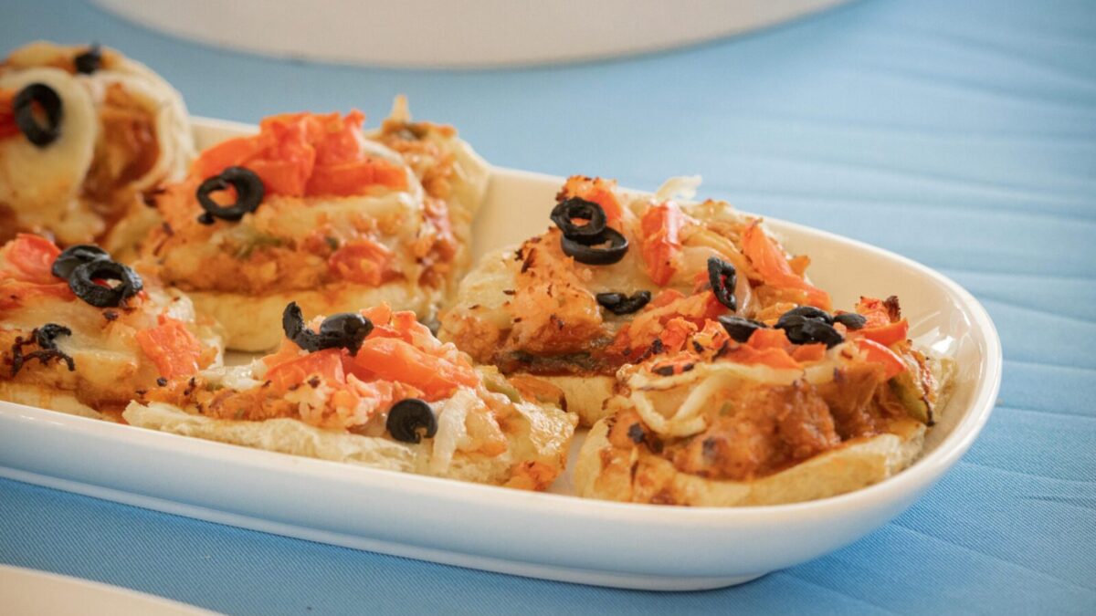 Delicious mini pizzas topped with black olives and tomatoes on a white dish.
