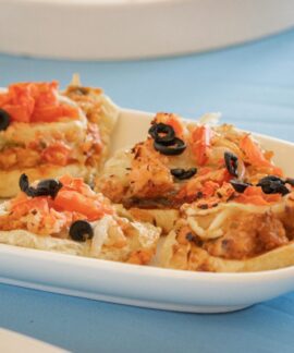 Delicious mini pizzas topped with black olives and tomatoes on a white dish.