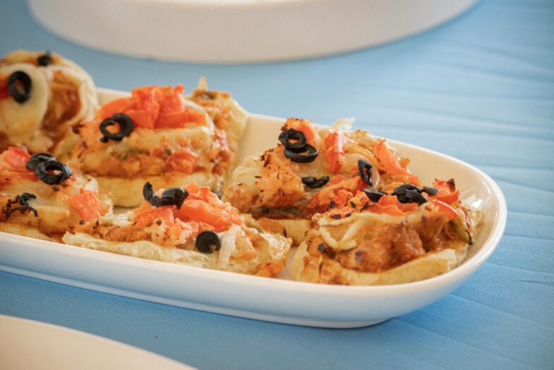 Delicious mini pizzas topped with black olives and tomatoes on a white dish.