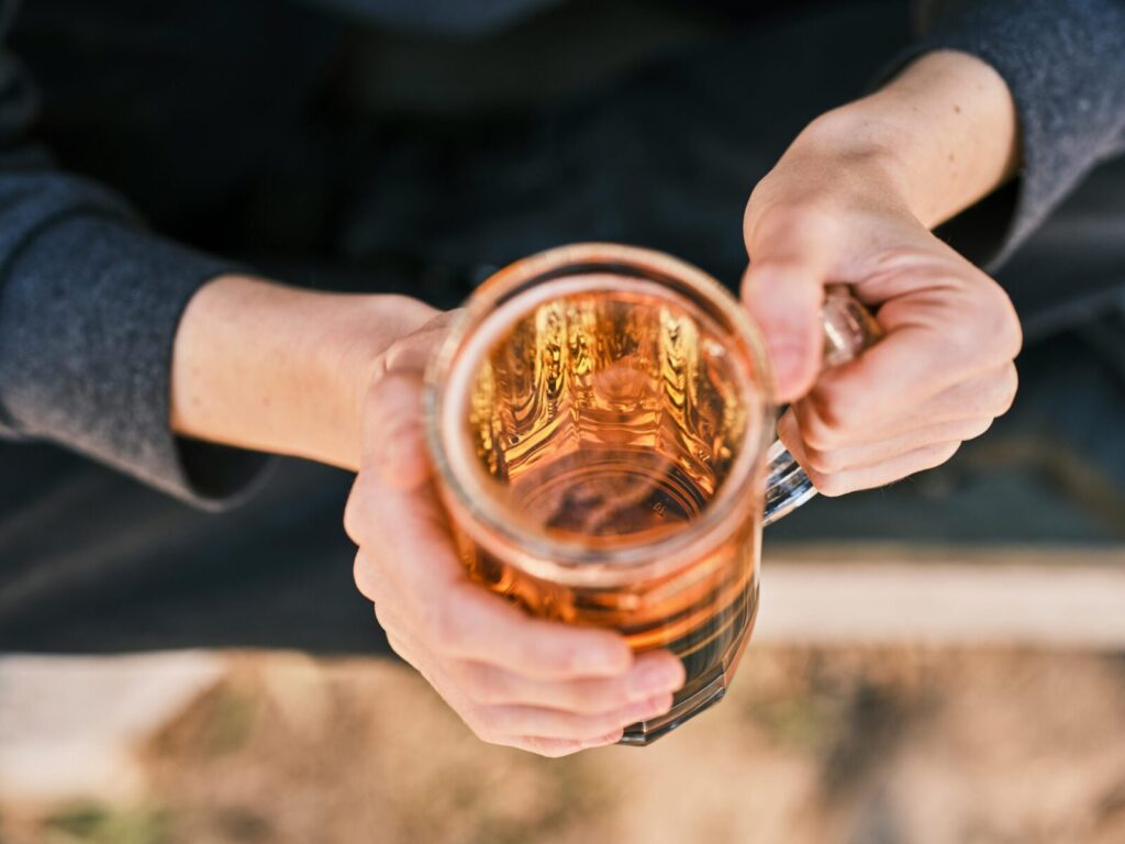 Close-up of hands holding a glass mug filled with amber beer, viewed from above.
