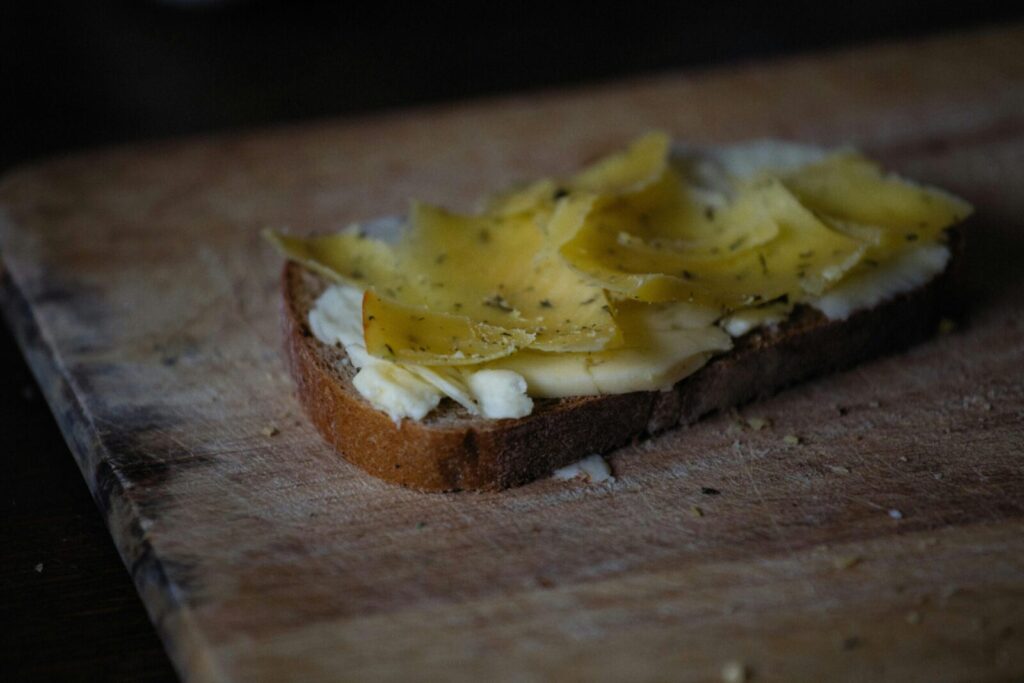 Close-up of rustic bread topped with butter and cheese slices on wooden board, perfect for breakfast or snack.