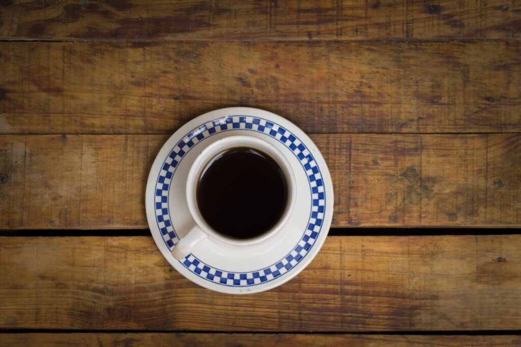 Aerial view of a coffee cup with a checkered saucer on a rustic wooden table.