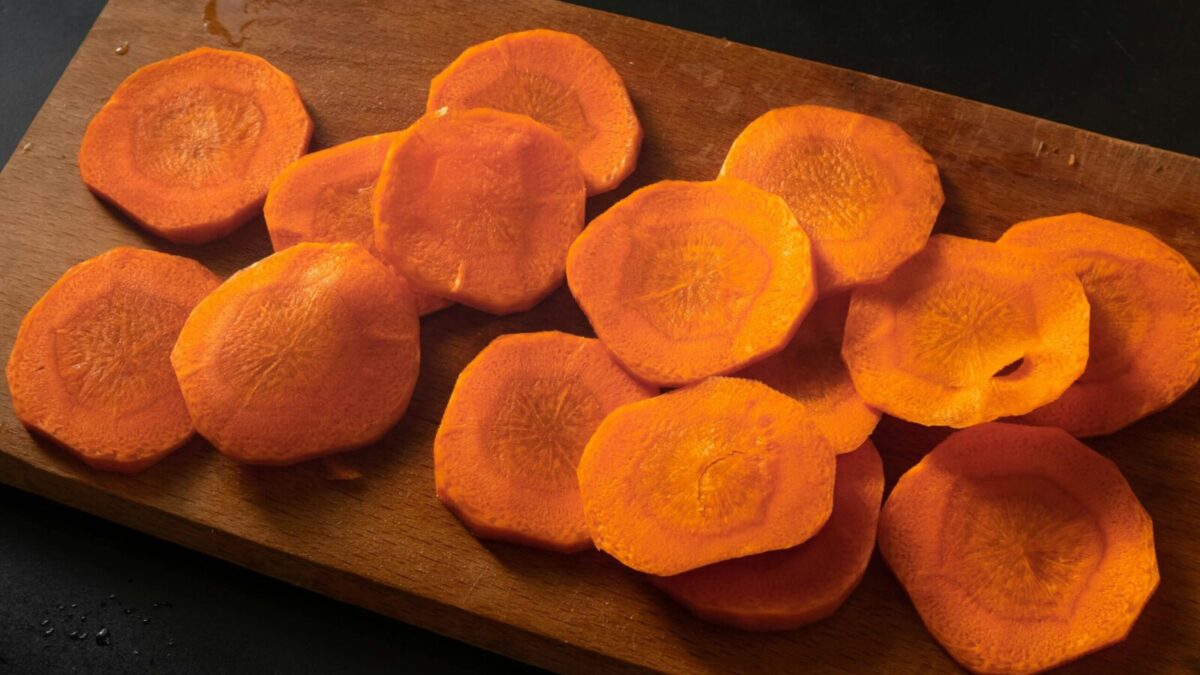 Freshly sliced carrots neatly arranged on a wooden chopping board.