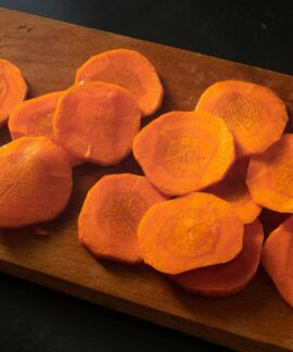 Freshly sliced carrots neatly arranged on a wooden chopping board.