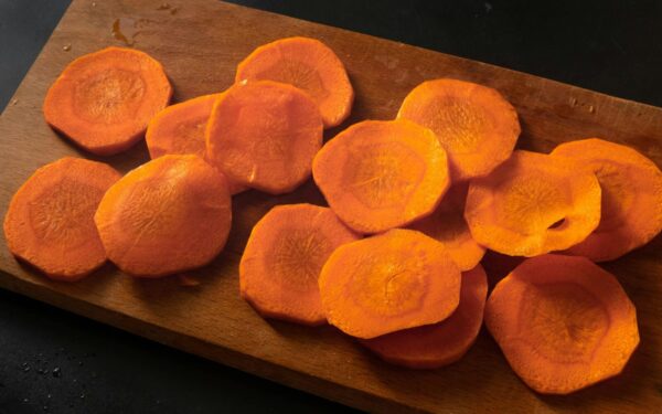 Freshly sliced carrots neatly arranged on a wooden chopping board.