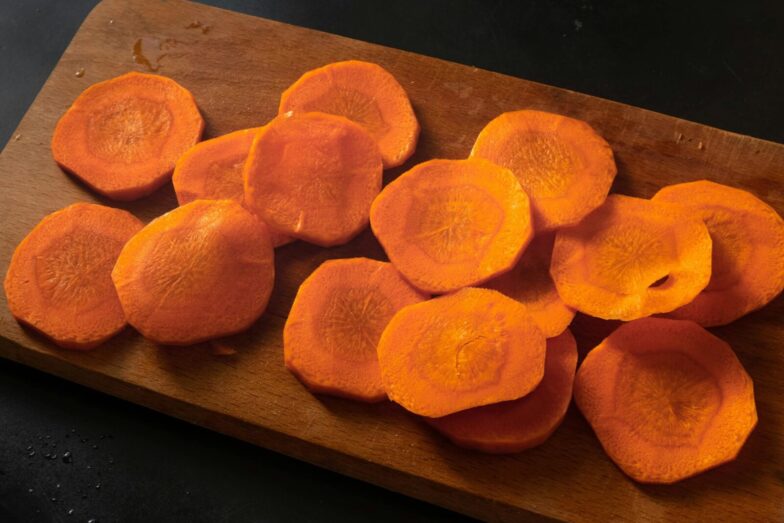 Freshly sliced carrots neatly arranged on a wooden chopping board.