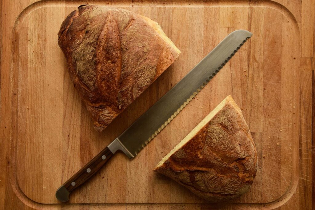 Sliced loaf of crusty bread with bread knife on a wooden cutting board, flat lay image.