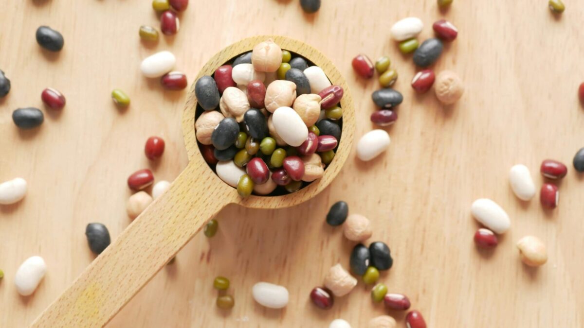 Close-up of assorted beans and legumes on a wooden spoon, showcasing diversity in food ingredients.
