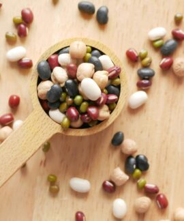 Close-up of assorted beans and legumes on a wooden spoon, showcasing diversity in food ingredients.