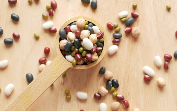 Close-up of assorted beans and legumes on a wooden spoon, showcasing diversity in food ingredients.