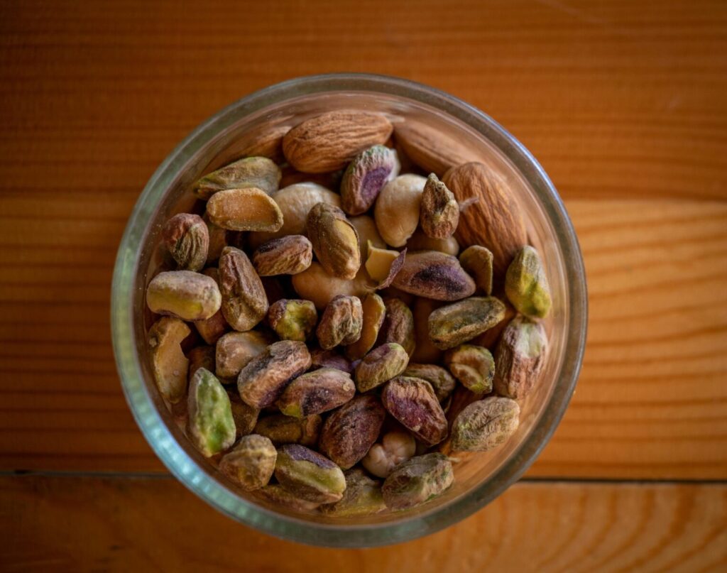 A close-up top view of assorted nuts in a glass bowl on a wooden table, highlighting natural textures.
