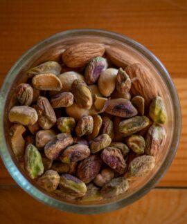 A close-up top view of assorted nuts in a glass bowl on a wooden table, highlighting natural textures.