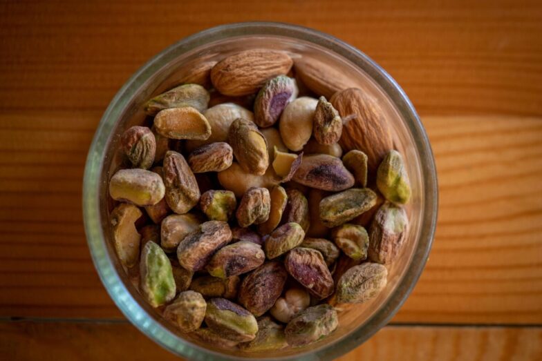 A close-up top view of assorted nuts in a glass bowl on a wooden table, highlighting natural textures.