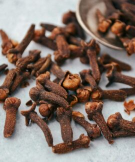 A close-up image of aromatic dry cloves scattered on a spoon over a gray surface.