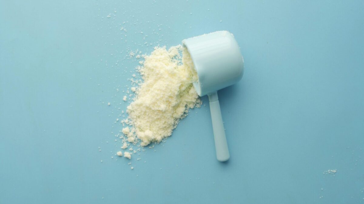 White powder spilled from a scoop on bright blue background. Clean and minimalistic food photo.