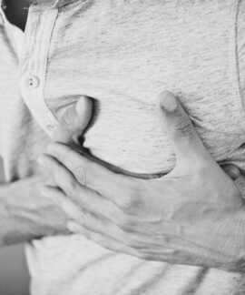 Black and white photo of a man clutching his chest, indicating discomfort or pain.