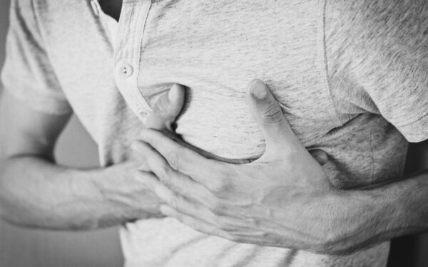 Black and white photo of a man clutching his chest, indicating discomfort or pain.