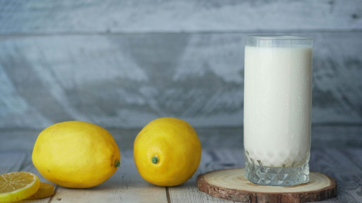 A close-up of fresh lemons and a glass of milk on a wooden table.