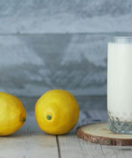A close-up of fresh lemons and a glass of milk on a wooden table.