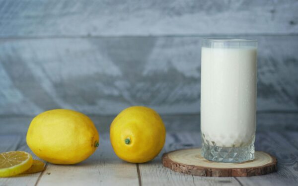 A close-up of fresh lemons and a glass of milk on a wooden table.