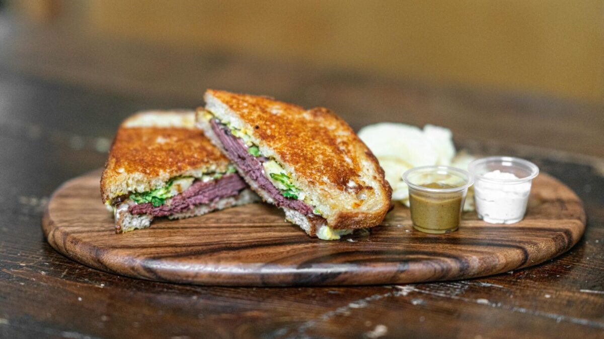 Delicious grilled sandwich with assorted dips on a rustic wooden tray, perfect for food lovers.