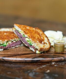 Delicious grilled sandwich with assorted dips on a rustic wooden tray, perfect for food lovers.