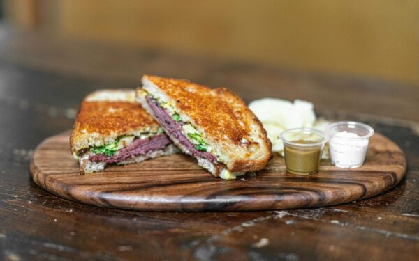 Delicious grilled sandwich with assorted dips on a rustic wooden tray, perfect for food lovers.