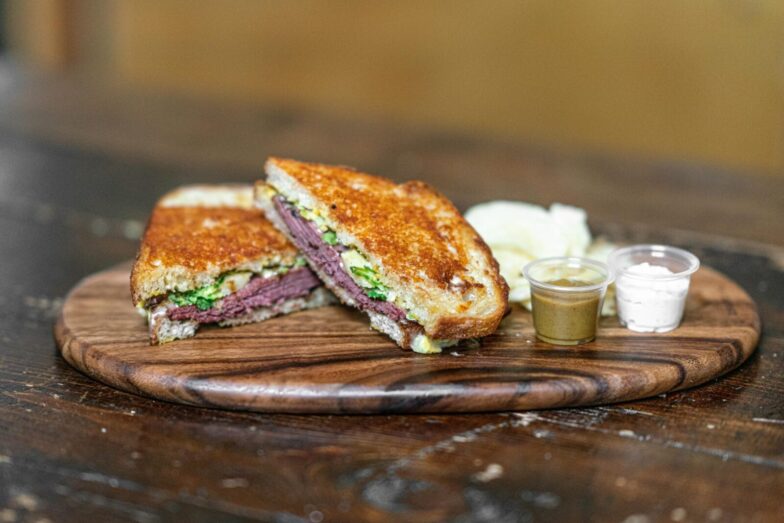 Delicious grilled sandwich with assorted dips on a rustic wooden tray, perfect for food lovers.
