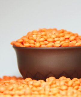 A focused image of a bowl filled with vibrant red lentils against a plain background.