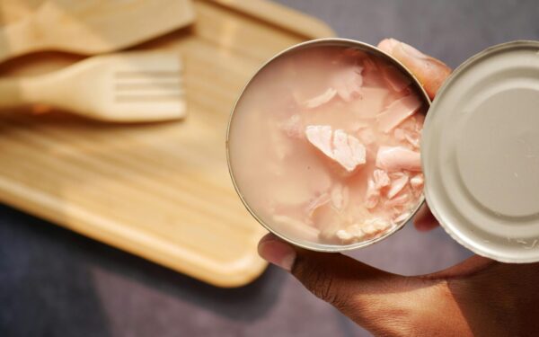 A close-up of an opened canned tuna held over a wooden cutting board and utensils.