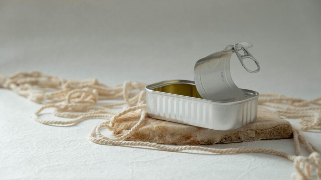 An open metal can rests artfully on a rock surrounded by string, creating a minimalist composition.