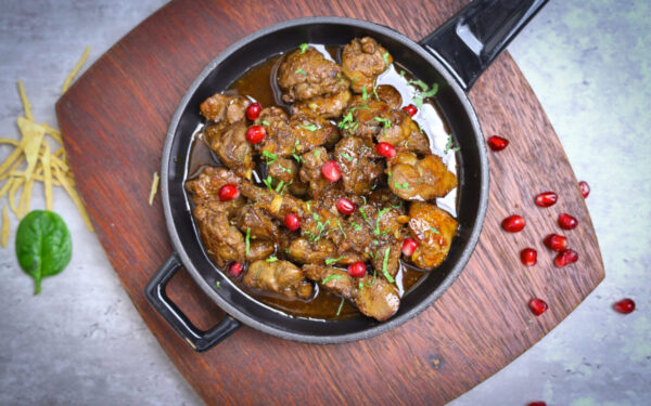 Delicious meat stew served with pomegranate seeds in a rustic pan.
