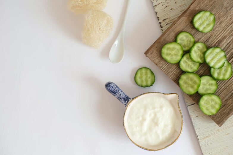 Top view of fresh cucumber slices and creamy yogurt on a rustic wooden board, ideal for healthy eating concepts.