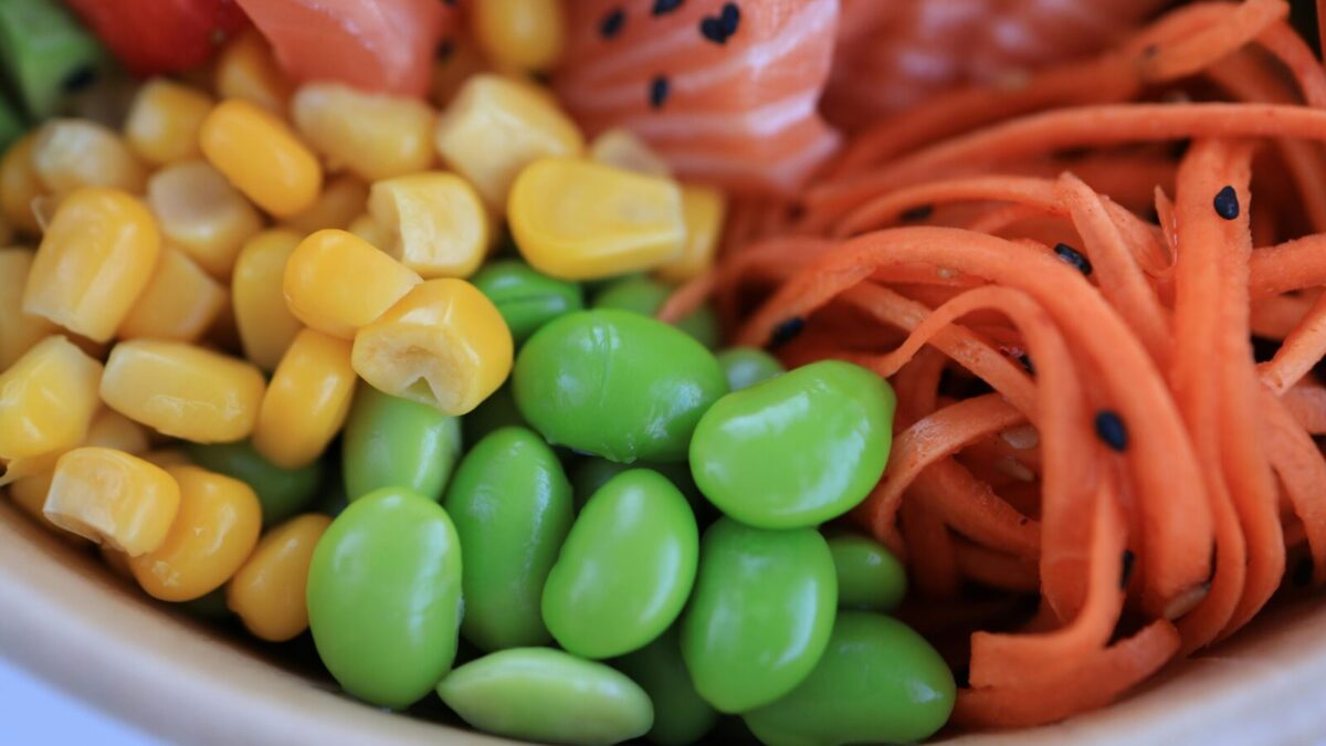 A vibrant close-up of salmon poke bowl with corn, edamame, and carrots.