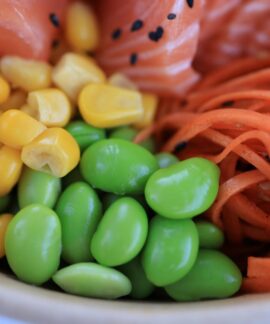 A vibrant close-up of salmon poke bowl with corn, edamame, and carrots.