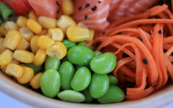 A vibrant close-up of salmon poke bowl with corn, edamame, and carrots.