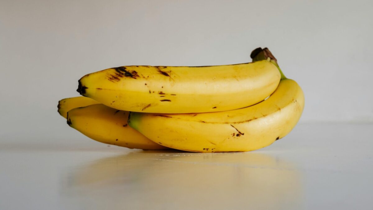 A bunch of fresh yellow bananas stacked elegantly on a smooth white surface, ready to eat.