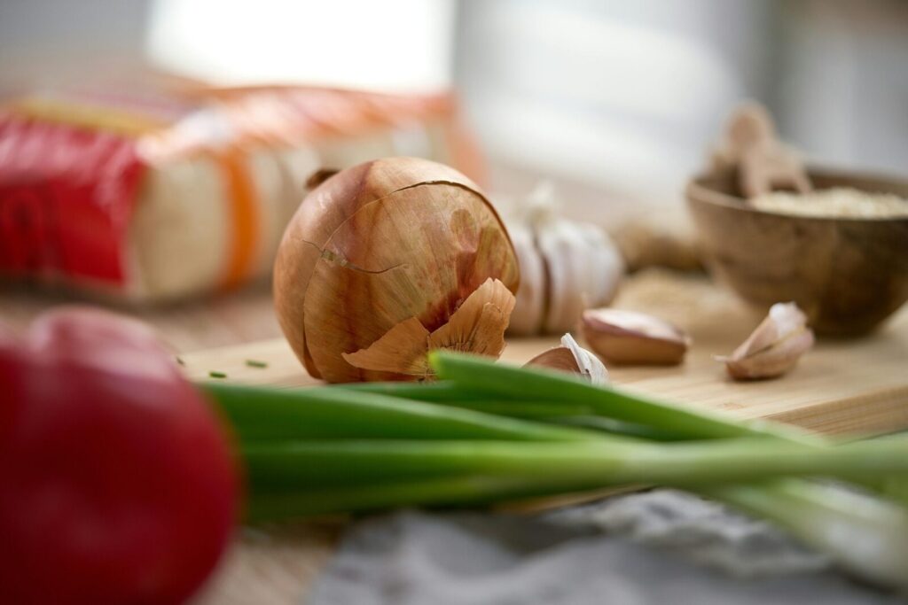 Close-up of fresh onions, garlic, and peppers on a rustic kitchen table, perfect for culinary themes.